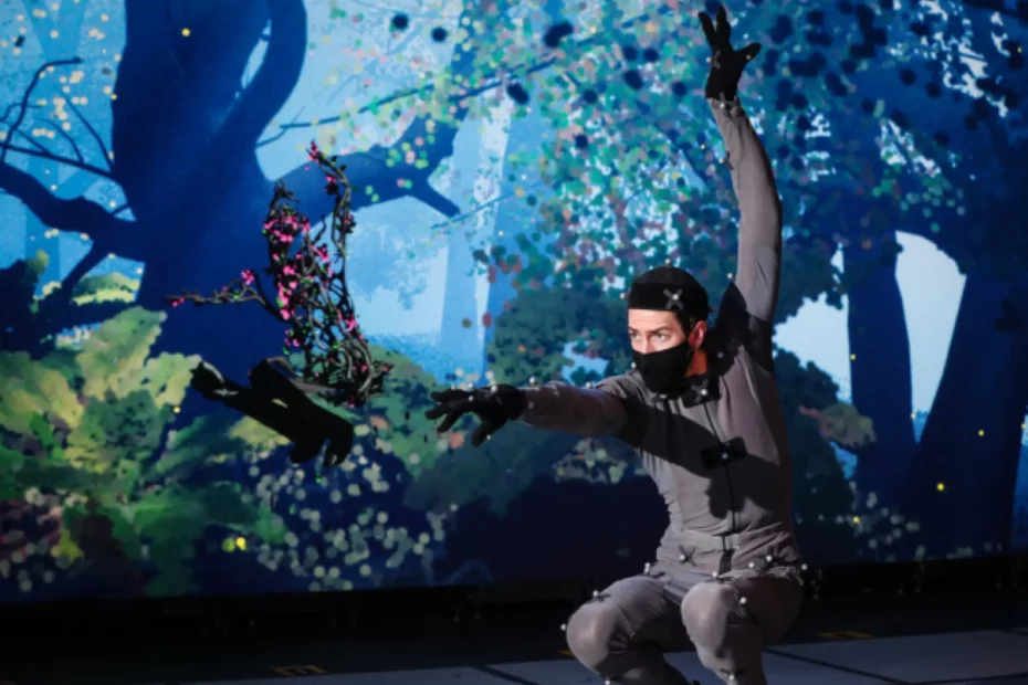 person in grey body suit moving past stage scene of forest