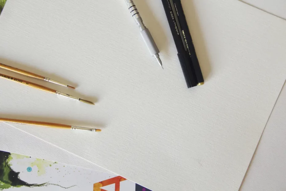 artist brushes and pens sat on large piece of white card