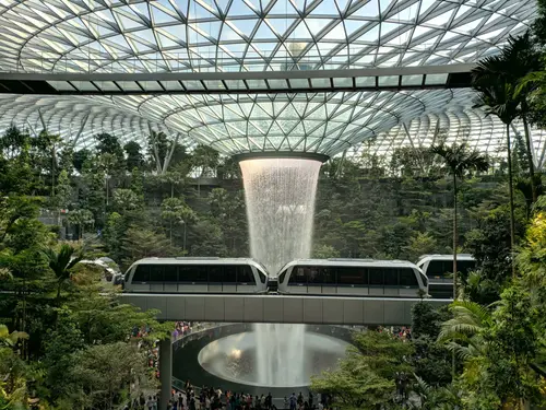 inside large glass building with trees, water feature and monor rail